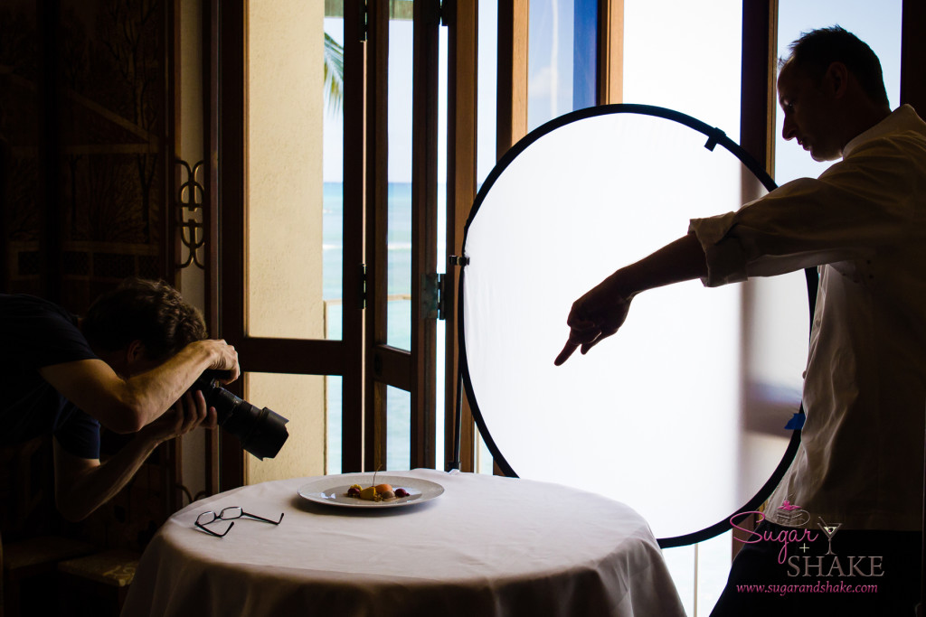 Pastry Chef Mark Freischmidt, Halekulani Hotel, points at a plate on a small table while a photographer takes a photo of the dish. © 2014 Sugar + Shake
