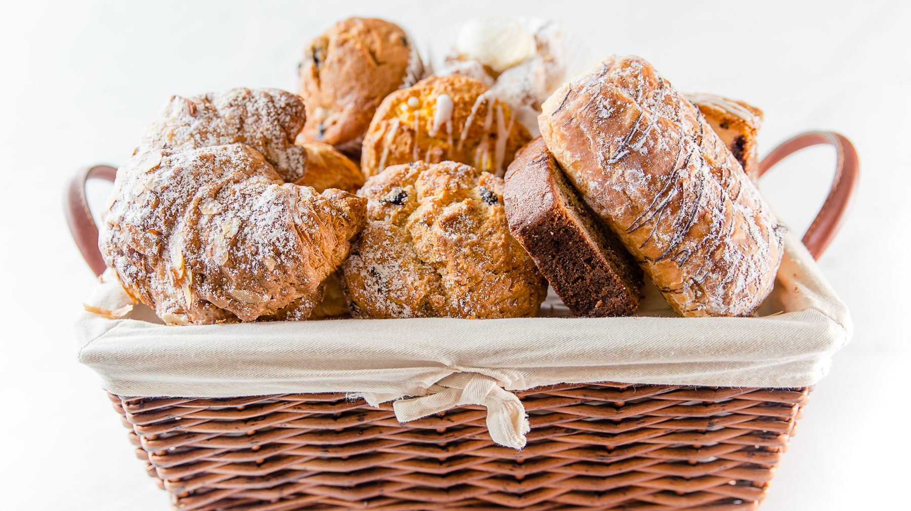 A wicker basket with a white liner basket liner filled with assorted pastry items